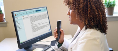 En kvinn i en hvit frakk som holder en telefon og ser på en dataskjerm.