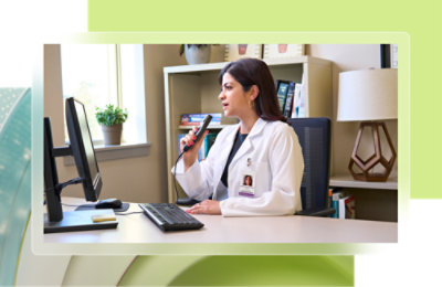 Une femme en blouse blanche regardant un écran d’ordinateur et parlant dans un microphone.