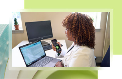 En kvinne som holder en telefon og ser på en bærbar datamaskin.