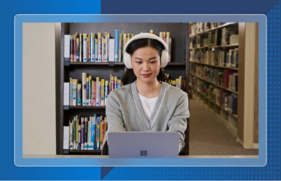 Person using a laptop with headphones in a library setting.