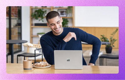 A man sitting at a table looking at a laptop with a logo on the wall in the background.