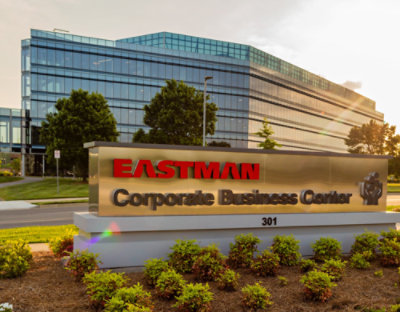 A sign with red text reading EASTMAN Corporate Business 301 next to a tree with green leaves.