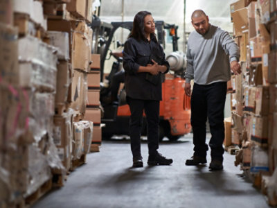 Workers reviewing inventory in warehouse aisle with forklift.
