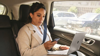Person using phone and laptop while seated in car.