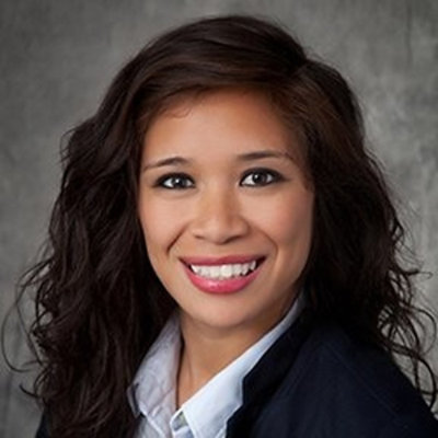 Close-up portrait of a person with long wavy hair in business attire smiling against a neutral background.