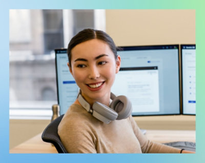 A woman wearing headphones around her neck, sitting in front of a computer.