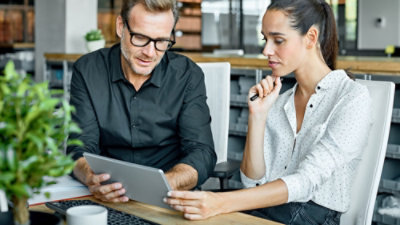 A man in a black shirt and glasses looking at a tablet.