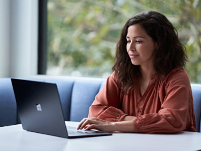 A woman in a red blouse sitting at a table using a laptop.