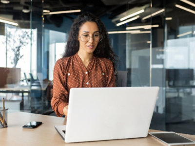 A woman in glasses looking at a laptop on a desk.