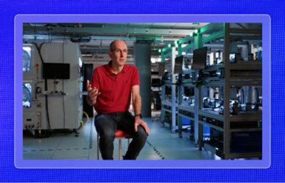 Person speaking in a technology lab with computing equipment in the background.