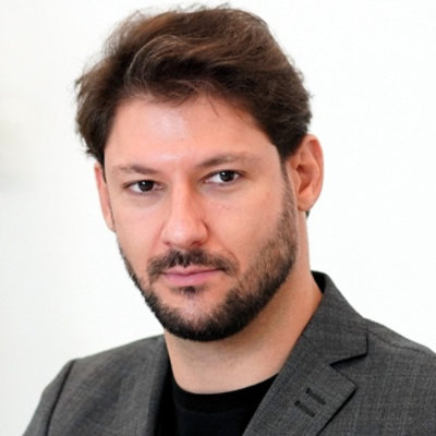 Headshot of person in a grey blazer and black shirt on a plain background
