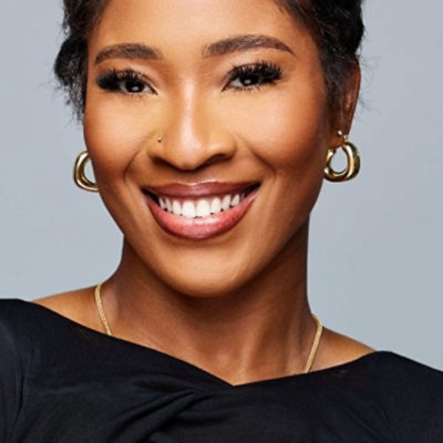 Headshot of person smiling, wearing earrings on a plain background