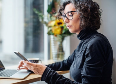 A woman with curly hair wearing glasses looking at her phone.