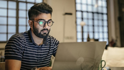 A man with glasses and a beard looking at a laptop.