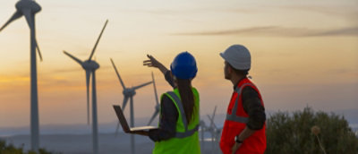 A man and woman in safety vests and hardhats looking at windmills.