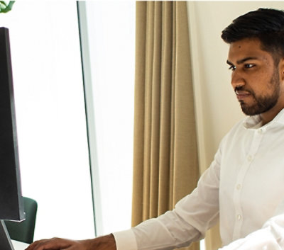 Ein Mann, der an einem Schreibtisch sitzt, und einen Computer mit لا auf dem Bildschirm verwendet.