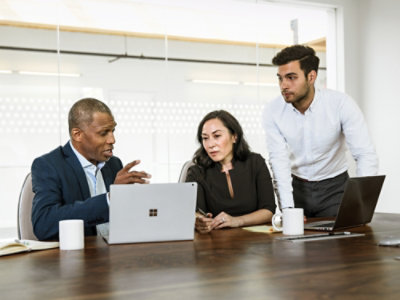 Mehrere Personen sitzen um einen Tisch und schauen auf einen Laptop.