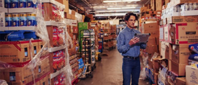 A man standing in a grocery store and noting details on the tab.
