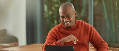 A man in a red sweater smiling at a laptop.