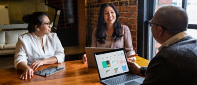 A woman sitting at a table and smiling at a laptop.