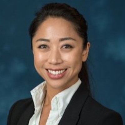 Professional headshot of a person in formal attire against a plain background.