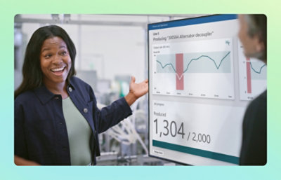 A woman in a blue jacket pointing at a screen displaying a graph.