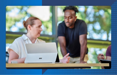 Two people discuss work at a table using a laptop, collaborating on tasks in a bright indoor setting.