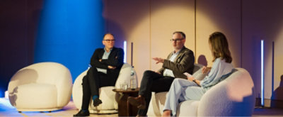 Panel discussion on stage with three speakers seated in chairs, sharing insights during a live event.