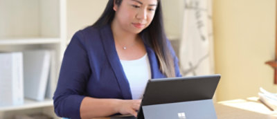 Person works on a tablet device at a desk, focused on tasks in a bright home or office setting.