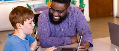 Teacher and student review work together on a laptop, collaborating in a classroom setting.