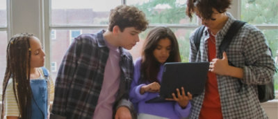 Group of students gather around a laptop, collaborating and reviewing content together in a learning space.