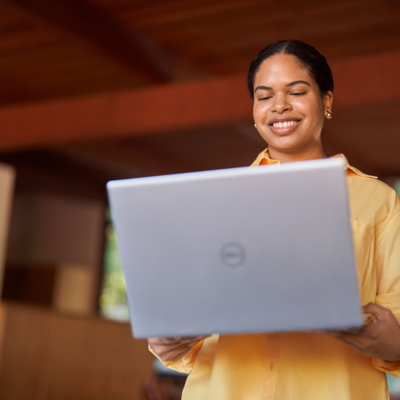 A young woman standing in a room with a laptop smiling