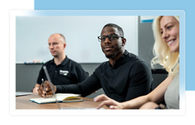 Tre persone sedute a un tavolo da conferenza, impegnate in una riunione. Una persona scrive su un blocco appunti.