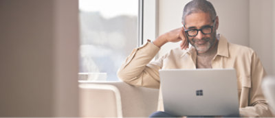 Uśmiechnięty mężczyzna w okularach używający laptopa Microsoft Surface.