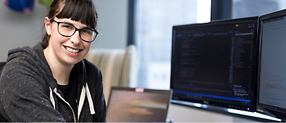 A woman in spectacles smiling and working on desktop