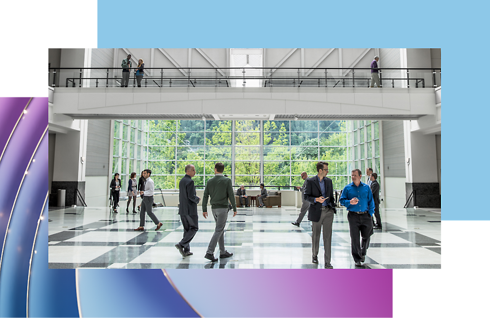 Modern office lobby with people walking and conversing, featuring a high glass ceiling and a reflective floor.