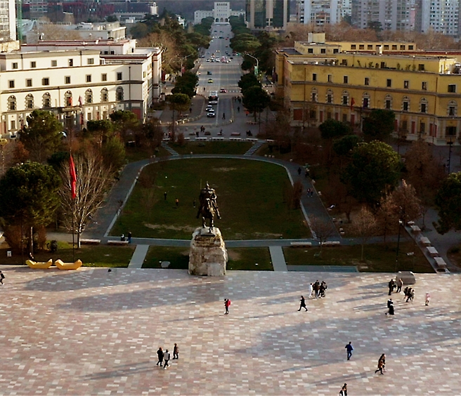Aerial view of a spacious city square with people walking, featuring a large equestrian statue and surrounding green park 