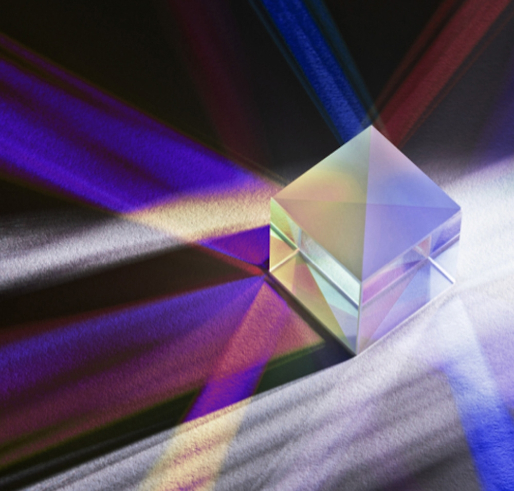 A glass prism on a surface, refracting light into a spectrum of colorful rays against a dark background.