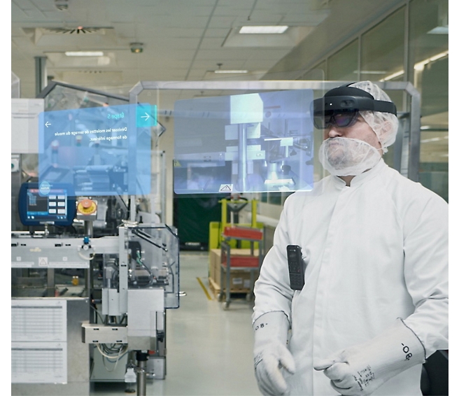 A man wearing a lab coat, hairnet, and augmented reality glasses stands in an industrial setting with virtual interfaces.