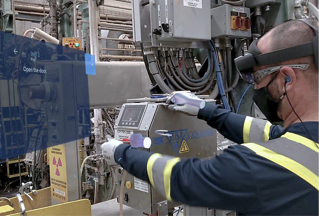 Een werknemer in een veiligheidsvest en met een headset maakt gebruik van een configuratiescherm in een industriële omgeving met complexe machines
