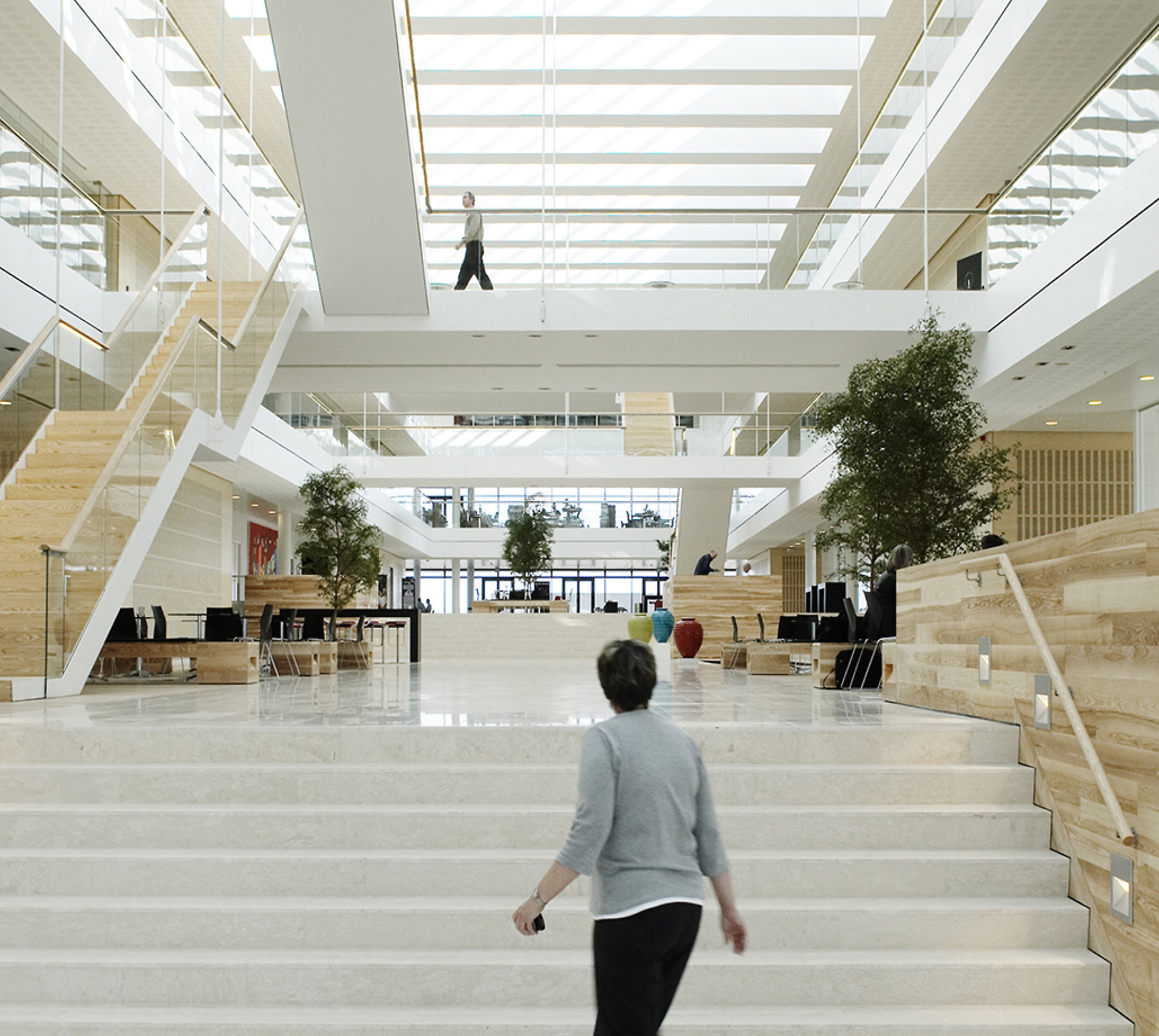 Modern office lobby with large white staircases, wooden accents, and people walking around. bright and airy atmosphere.