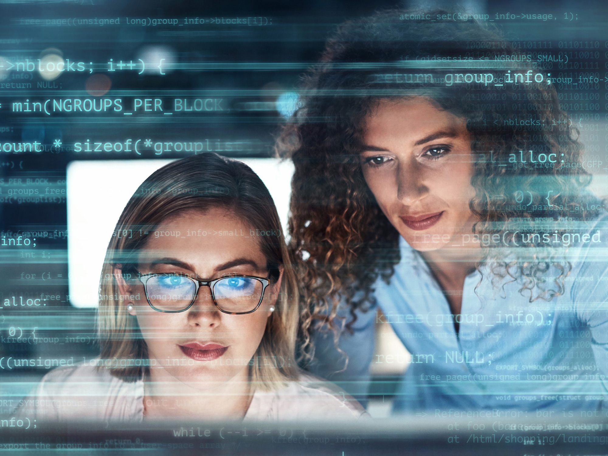 Two women working on computer programming with code overlayed across their faces, depicting a focus on technology 
