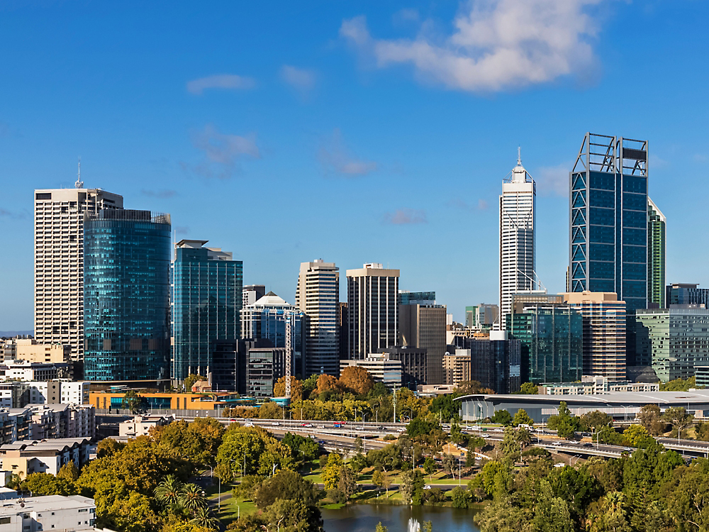 Austraalia Perthi siluett, kus on näha tänapäevased kõrghooned selge sinise taeva all, esiplaanil on lopsakas rohelus.