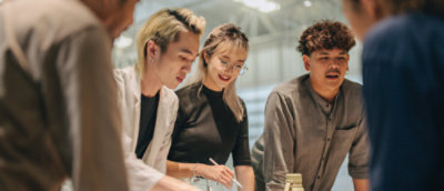 A group of people standing and discussing, looking over a desk