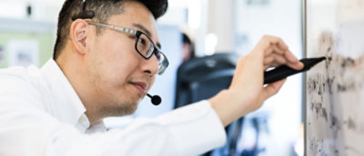 ผู้ชายใส่ชุดหูฟังกําลังเขียนบนไวท์บอร์ดในสํานักงาน