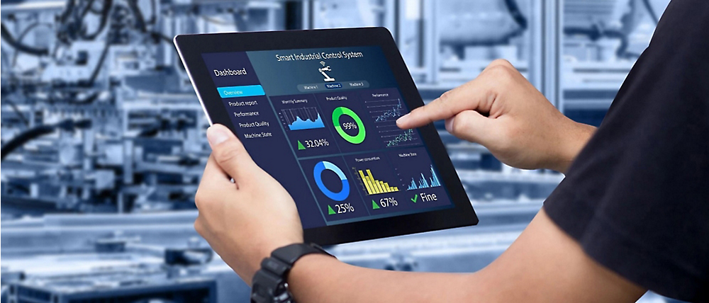 Bulanık bir endüstriyel arka plan önünde çeşitli analizlerin gösterildiği dijital tableti kullanan bir kişi.