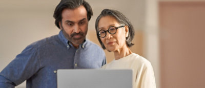 Muškarac srednjih godina i starija žena zajedno gledaju u ekran laptopa, verovatno razgovarajući o njegovom sadržaju.