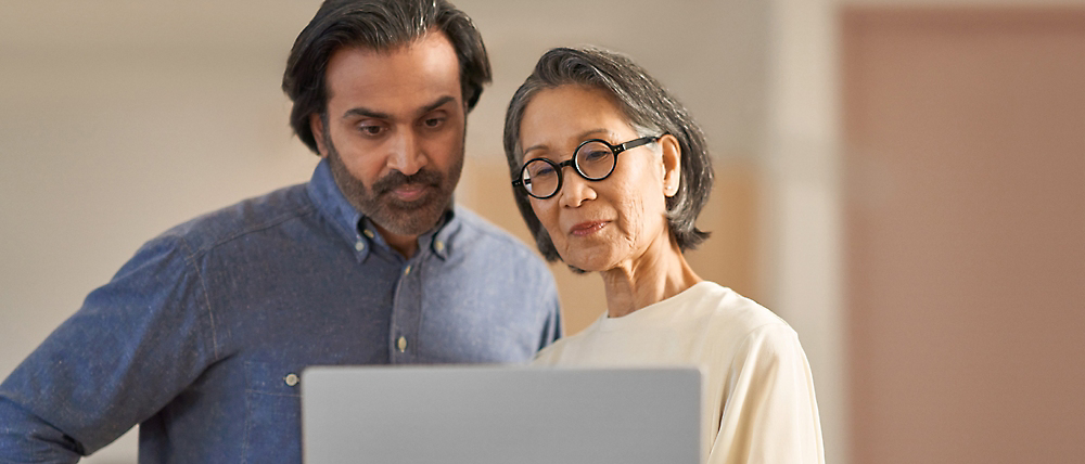 Un hombre de mediana edad y una mujer mayor mirando juntos una pantalla de un portátil, posiblemente hablando de su contenido.