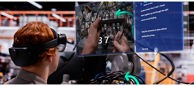 仮想現実ヘッドセットを装着している技術者が、デジタル オーバーレイ ガイドを参照しながら電気パネルで作業している。
