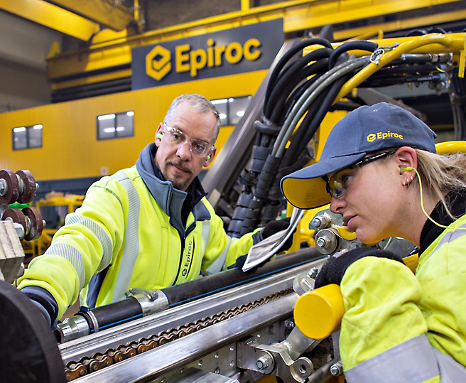Two technicians wearing high-visibility jackets working on industrial machinery in an epiroc facility.